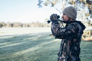 Adult male in camouflage outfit using binoculars in an open field, showcasing outdoor exploration and observation.